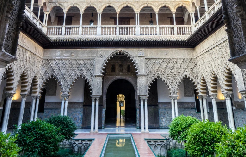 Cour intérieure mudéjare de l’Alcazar de Séville avec ses arches sculptées et son bassin central.